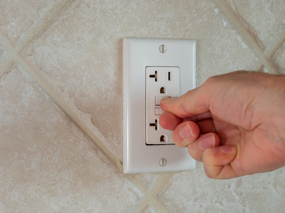 A hand resetting a GFCI outlet.